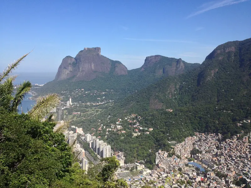 A Pedra da Gávea e a Pedra Bonita sobre a mata, vistas de longe, com o bairro de São Conrado abaixo.